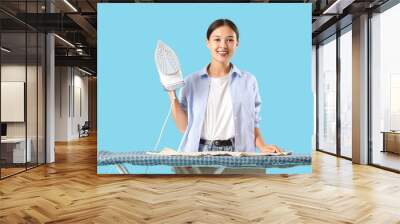 Young Asian woman ironing clothes on blue background Wall mural