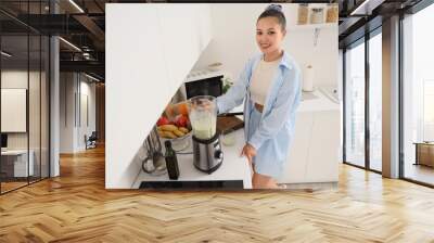 Young Asian woman making smoothie with blender in kitchen Wall mural