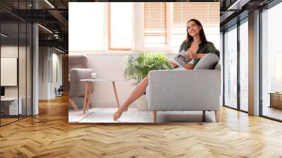 Young barefoot woman reading magazine on sofa at home Wall mural