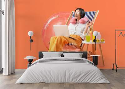 Young businesswoman with laptop and beach accessories ready for summer vacation on orange background Wall mural