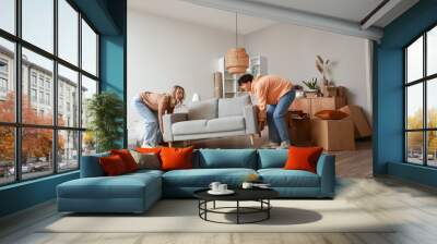 Young couple carrying sofa in room on moving day Wall mural