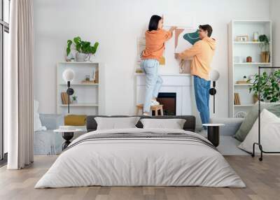 Young couple hanging paintings on light wall above fireplace at home, back view Wall mural