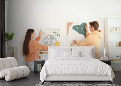 Young couple hanging paintings on wall above fireplace at home, back view Wall mural