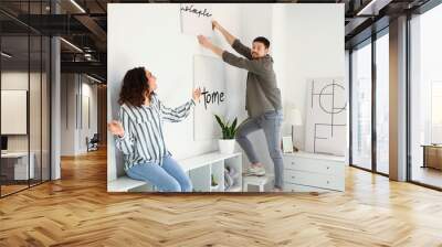 Young couple hanging poster on light wall at home Wall mural