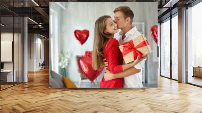 Young couple with gift box hugging at home Wall mural