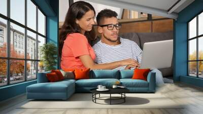 Young couple with laptop sitting on sofa at home Wall mural