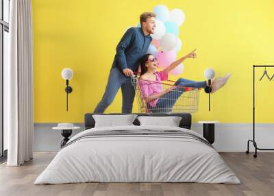 Young couple with shopping cart and balloons near color wall Wall mural