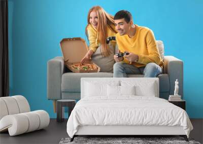 Young couple with tasty pizza playing video game on blue background Wall mural