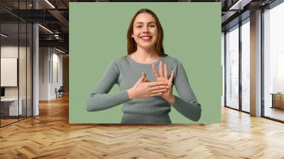 Young deaf mute woman using sign language on green background Wall mural