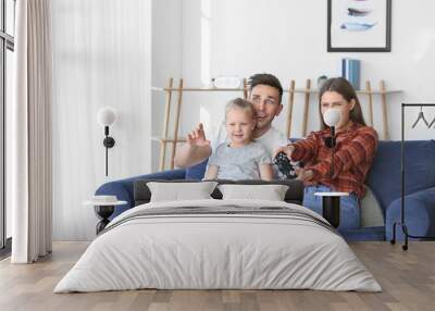 Young family playing video games while sitting on sofa at home Wall mural