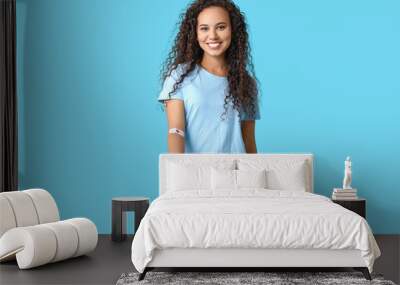 Young female African-American blood donor with applied medical patch and heart on blue background Wall mural