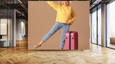 Young female tourist with suitcase waving hand on beige background Wall mural