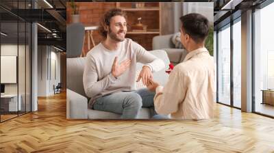 Young gay putting engagement ring on his boyfriend's finger at home Wall mural