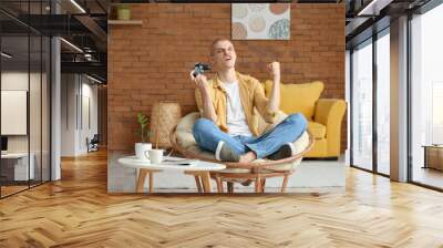 Young guy playing video game in armchair at home Wall mural