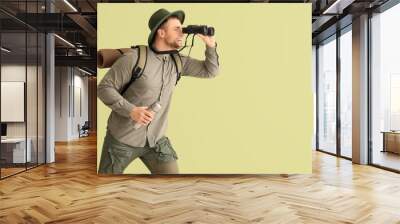 Young male tourist looking through binoculars on green background Wall mural