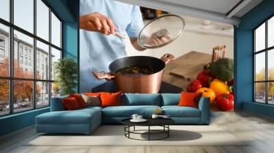 Young man cooking soup at table in kitchen Wall mural