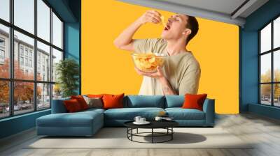 Young man eating tasty potato chips on yellow background Wall mural