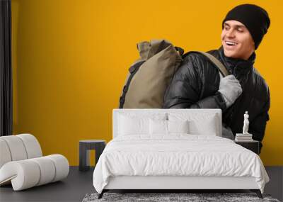 Young man in black stylish puffer jacket and hat with bag on yellow background Wall mural