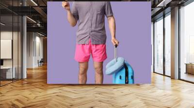 Young man in hat and sunglasses with suitcase and credit card on lilac background Wall mural