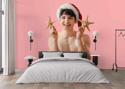 Young man in Santa hat with starfishes on pink background. Christmas in July Wall mural