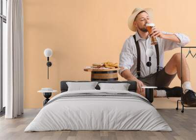 Young man in traditional German clothes drinking beer on beige background with space for text Wall mural