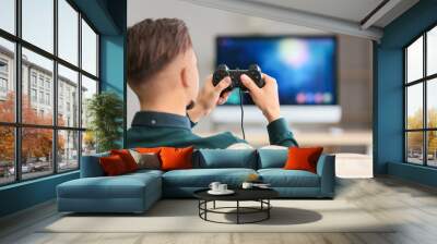 Young man playing video game at home Wall mural