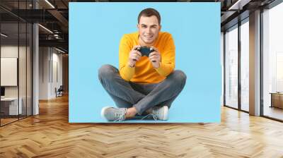 Young man playing video game on color background Wall mural