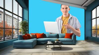 Young man pointing at laptop on blue background Wall mural