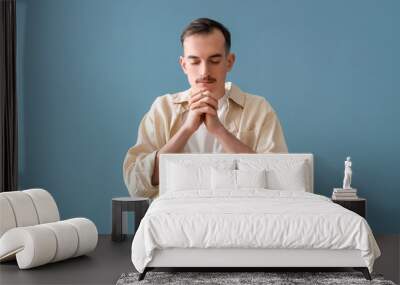 Young man praying on blue background Wall mural