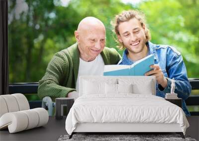 Young man reading book to his elderly father in park Wall mural