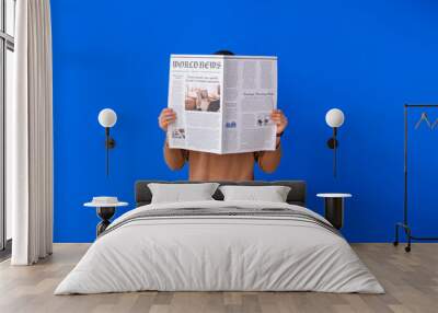 Young man reading newspaper on color background Wall mural