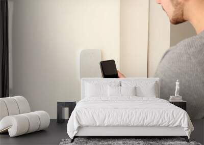 Young man setting alarm system with mobile phone, indoors Wall mural