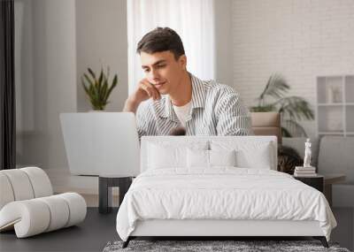 Young man using laptop at table with cute cat in home office Wall mural