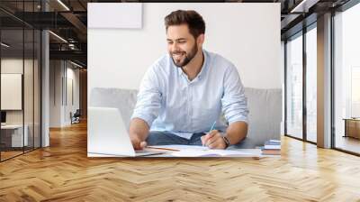 Young man using laptop for online learning at home Wall mural