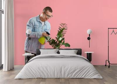 Young man watering plant with money on pink background Wall mural