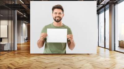 Young man with blank paper sheet on light background Wall mural