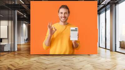 Young man with calculator showing OK gesture on color background Wall mural