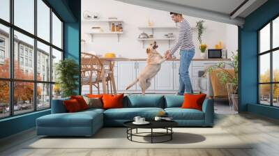 Young man with cute Labrador dog dancing in kitchen Wall mural