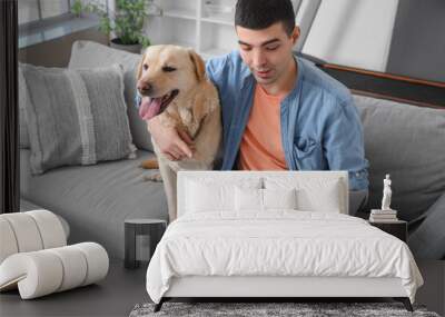 Young man with cute Labrador dog using laptop on sofa at home Wall mural