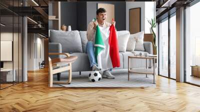 Young man with flag of Italy watching football game on TV at home Wall mural