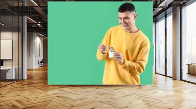 Young man with glass of tasty yogurt on green background Wall mural