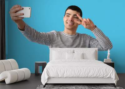 Young man with mobile phone taking selfie on blue background Wall mural