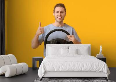 Young man with steering wheel showing thumb-up on color background Wall mural