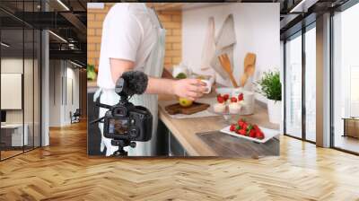 Young man with sweet muffins and fresh strawberries recording cooking video in kitchen Wall mural