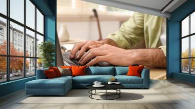 Young man working with laptop on table at home, closeup Wall mural