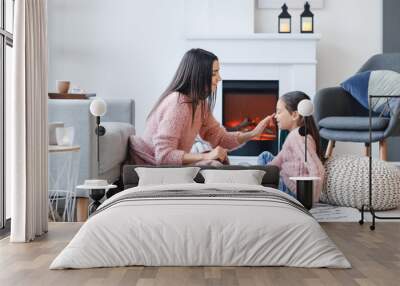 Young mother and daughter resting near fireplace at home Wall mural