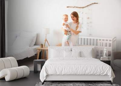 Young mother holding her cute little baby near crib in bedroom Wall mural