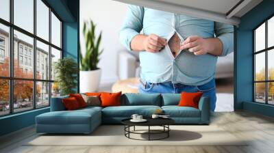 Young overweight man in tight shirt at home, closeup Wall mural