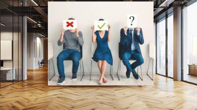 Young people holding paper sheets with different marks while sitting on chairs indoors. Job interview concept Wall mural