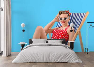 Young pin-up woman sitting in deck chair on blue background Wall mural